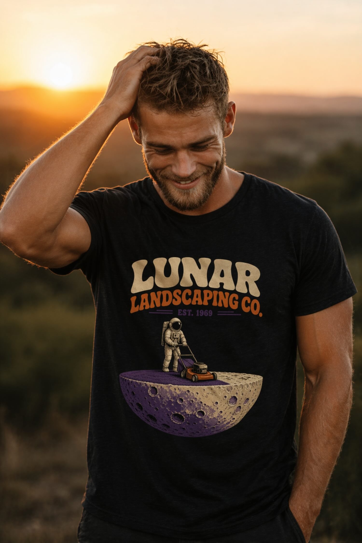Man modeling black graphic t-shirt with Lunar Landscaping Co. EST. 1969 astronaut mowing moon lawn design in golden hour sunset outdoor setting