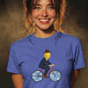 Woman with wavy brown hair smiling wearing blue t-shirt featuring lemon head in suit and bowler hat riding bicycle graphic design