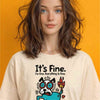 Woman with wavy brown hair wearing white "It's Fine. I'm Fine. Everything Is Fine." t-shirt featuring stressed cartoon dog on fire meme graphic