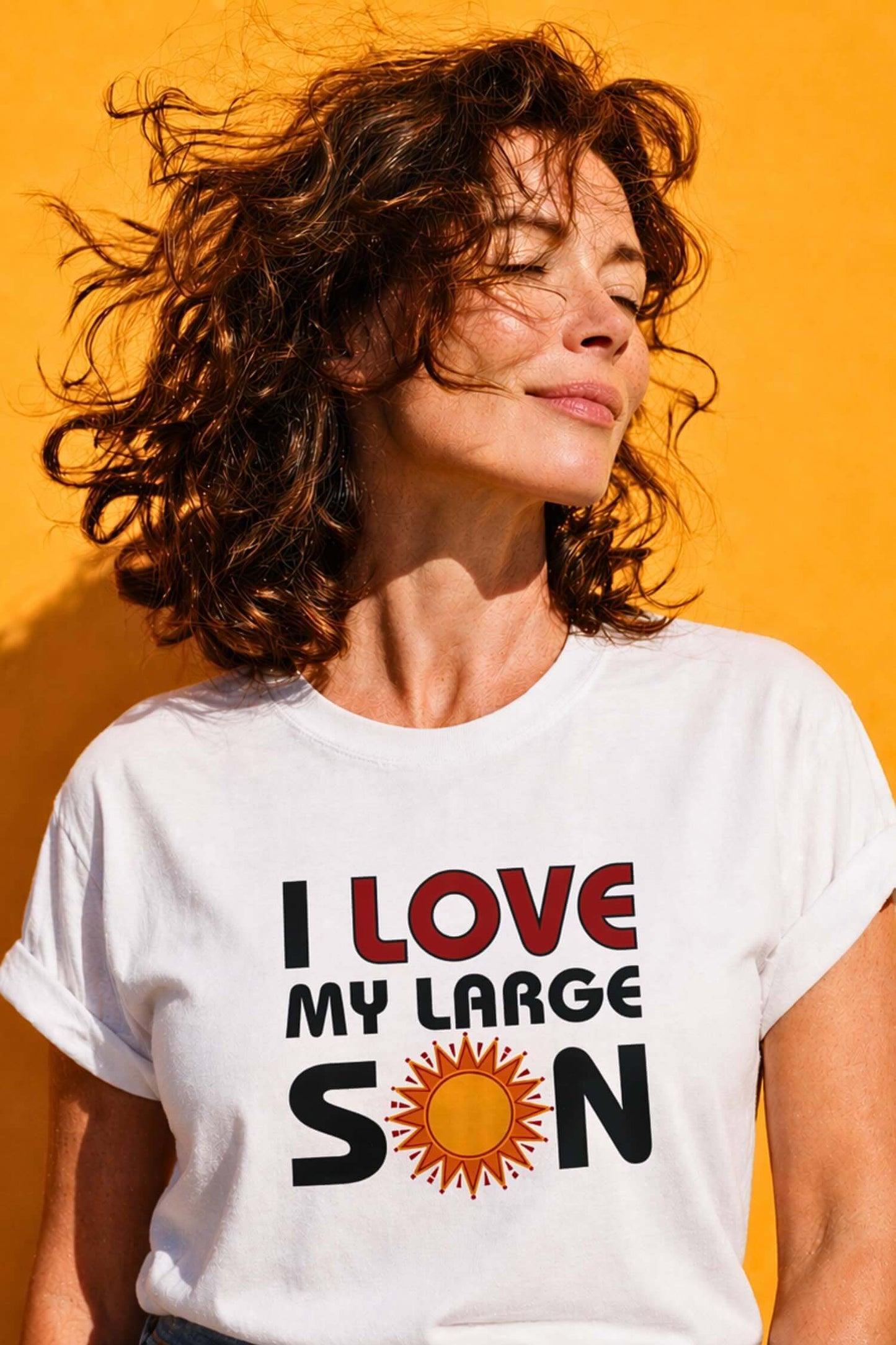 Woman with windswept wavy brown hair wearing white "I Love My Large Son" t-shirt with sun graphic
